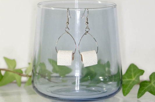 Miniature Toilet Paper Roll Earrings displayed on a glass.