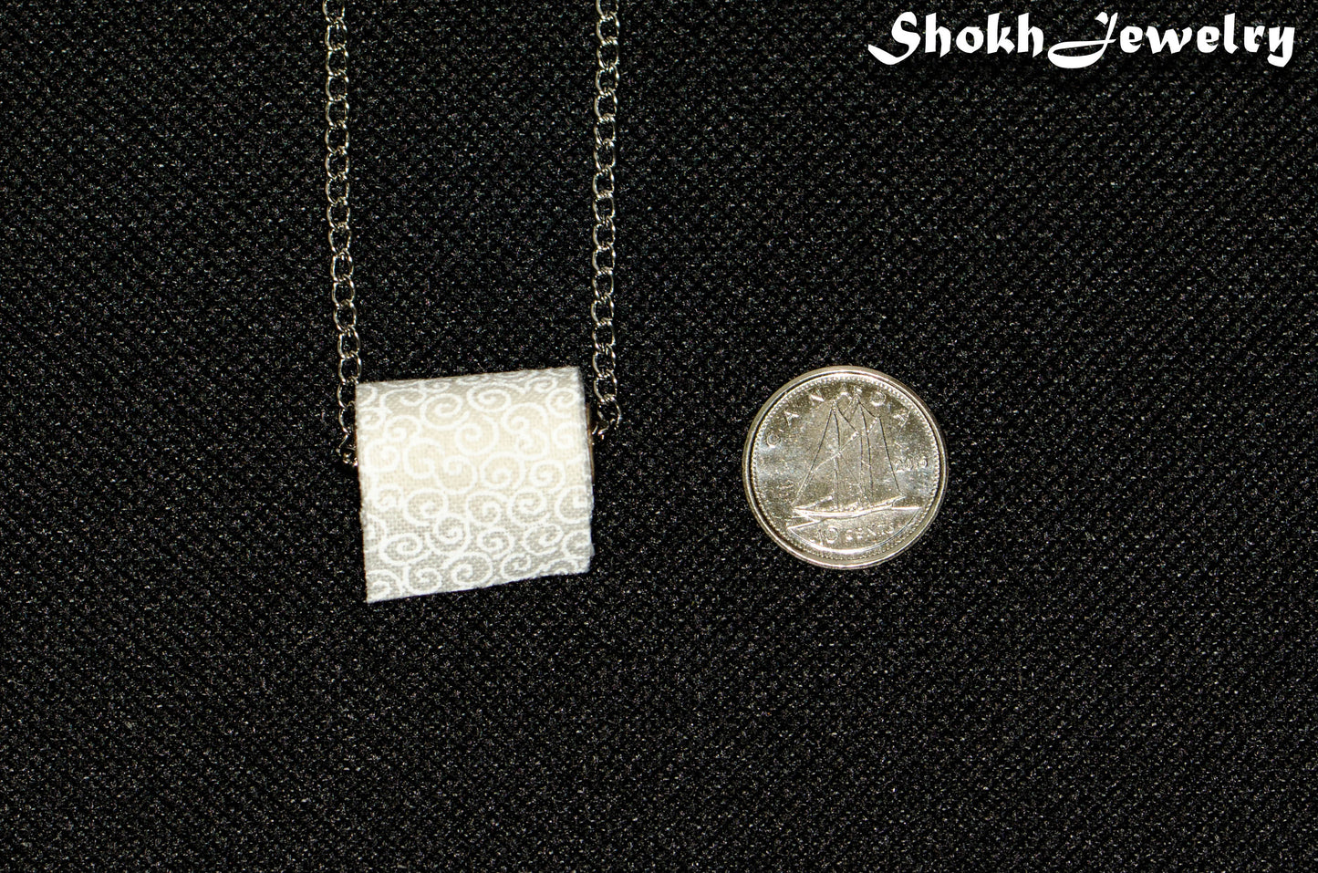Miniature Toilet Paper Roll Necklace beside a dime.