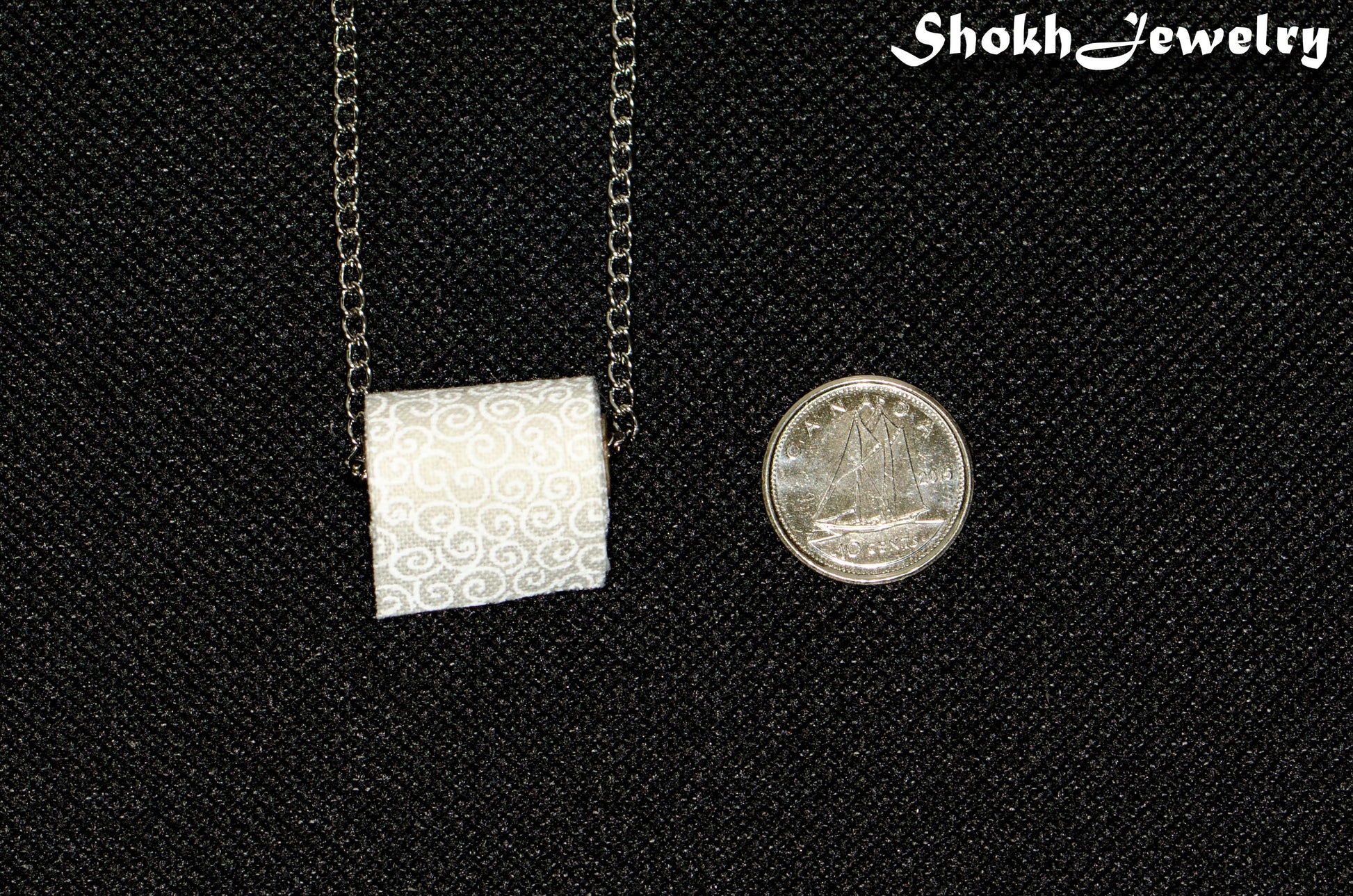 Miniature Toilet Paper Roll Necklace beside a dime.