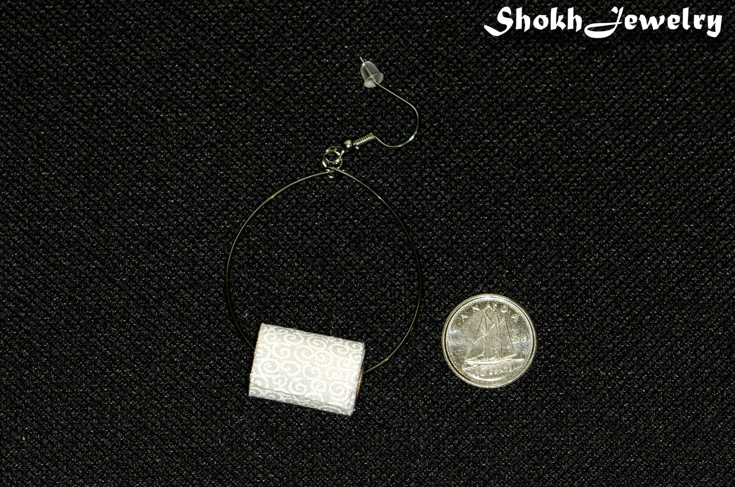 Miniature Toilet Paper Roll Earring beside a dime.