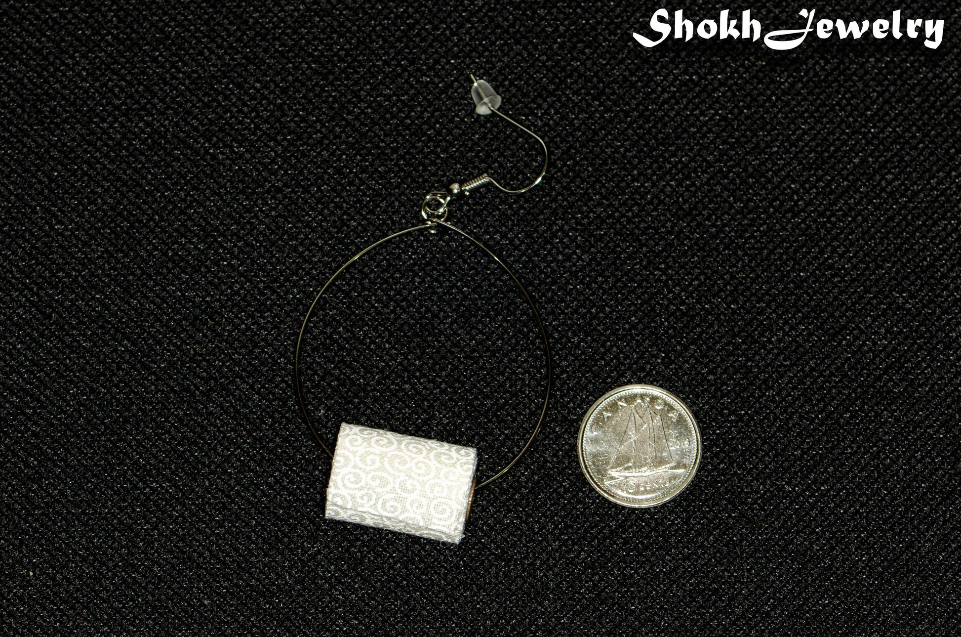 Miniature Toilet Paper Roll Earring beside a dime.