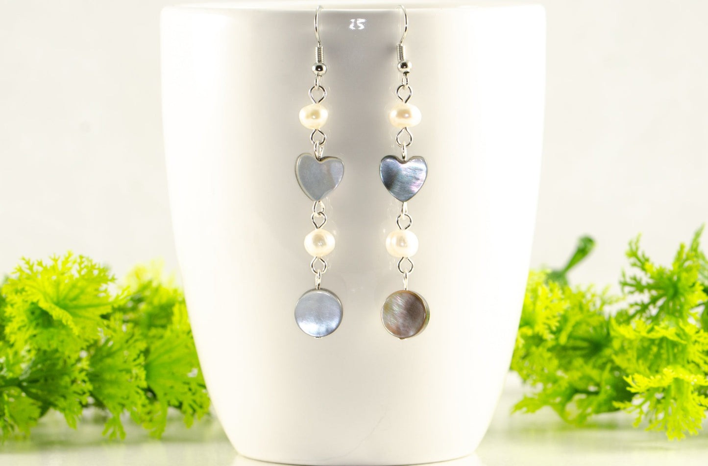 Long Grey Seashell and Freshwater Pearl Earrings displayed on a coffee mug.