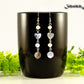 Long Grey Seashell and Freshwater Pearl Earrings displayed on a black coffee mug.