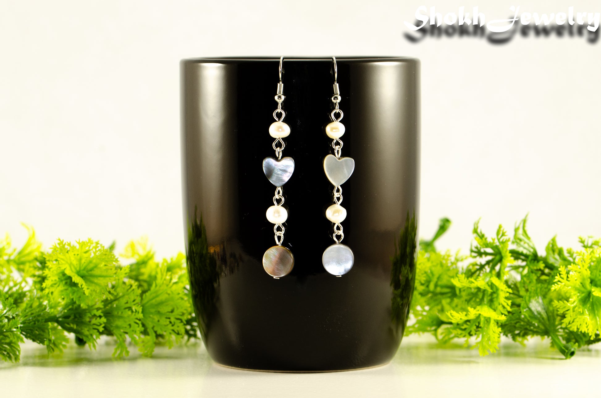 Long Grey Seashell and Freshwater Pearl Earrings displayed on a black coffee mug.