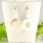 White Doughnut Seashell Earrings displayed on a tea cup.