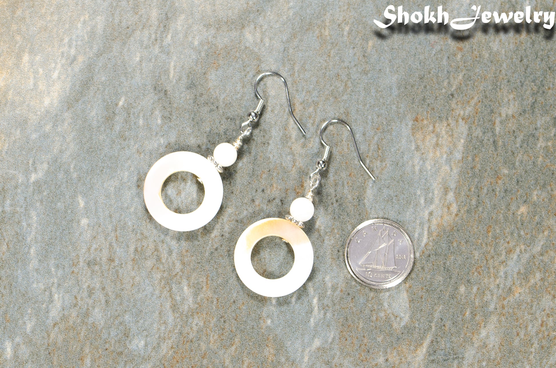 White Doughnut Seashell Earrings beside a dime.