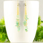 Long Gold Plated Chain and Green Aventurine Chip Earrings displayed on a coffee mug.