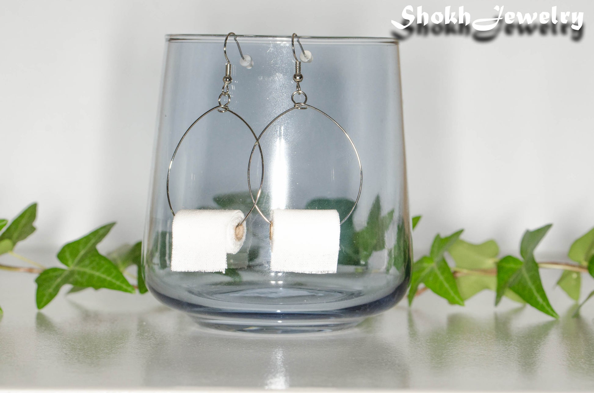Miniature Toilet Paper Roll Earrings displayed on a glass.