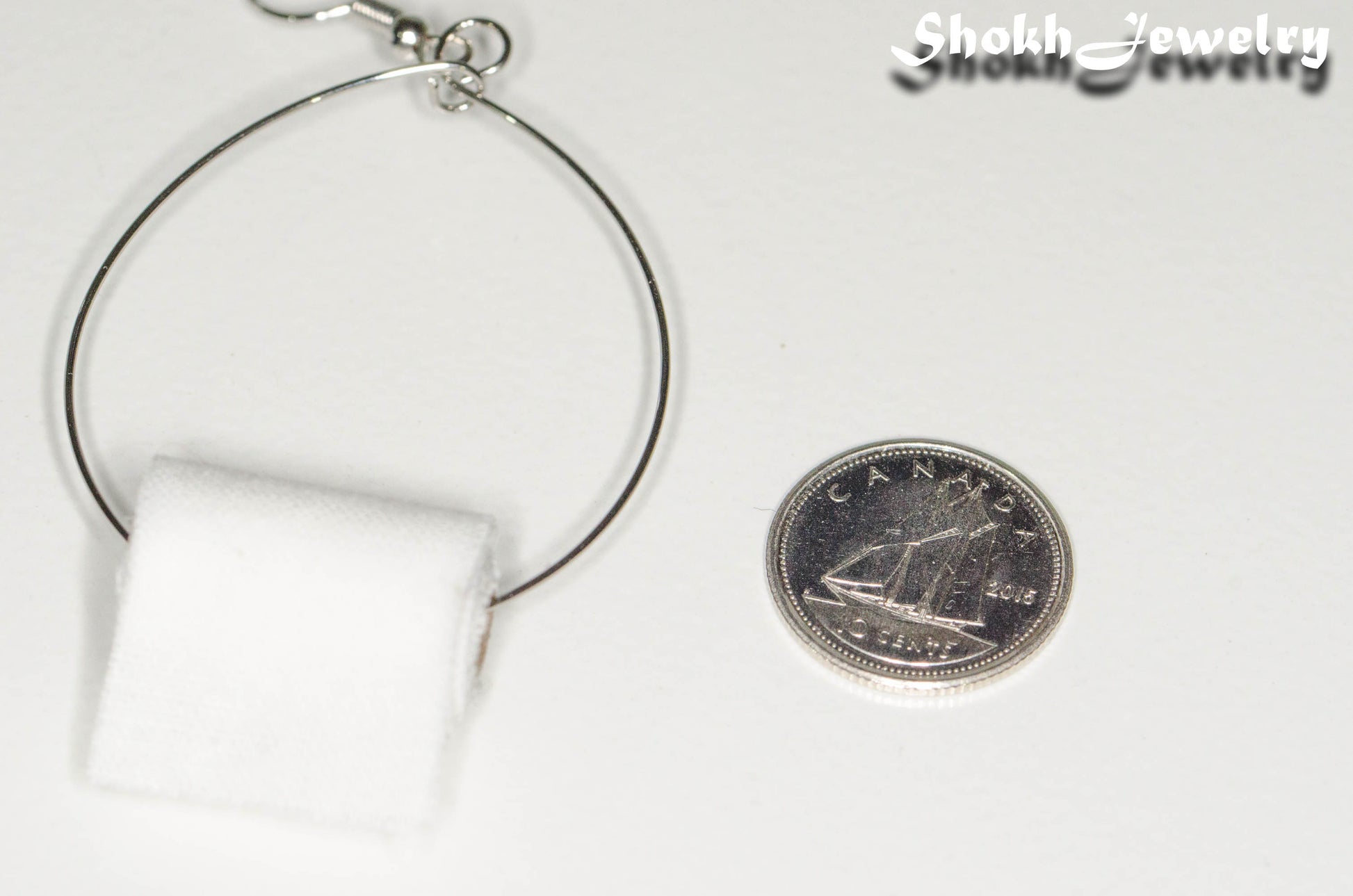 Miniature Toilet Paper Roll Earring beside a dime.