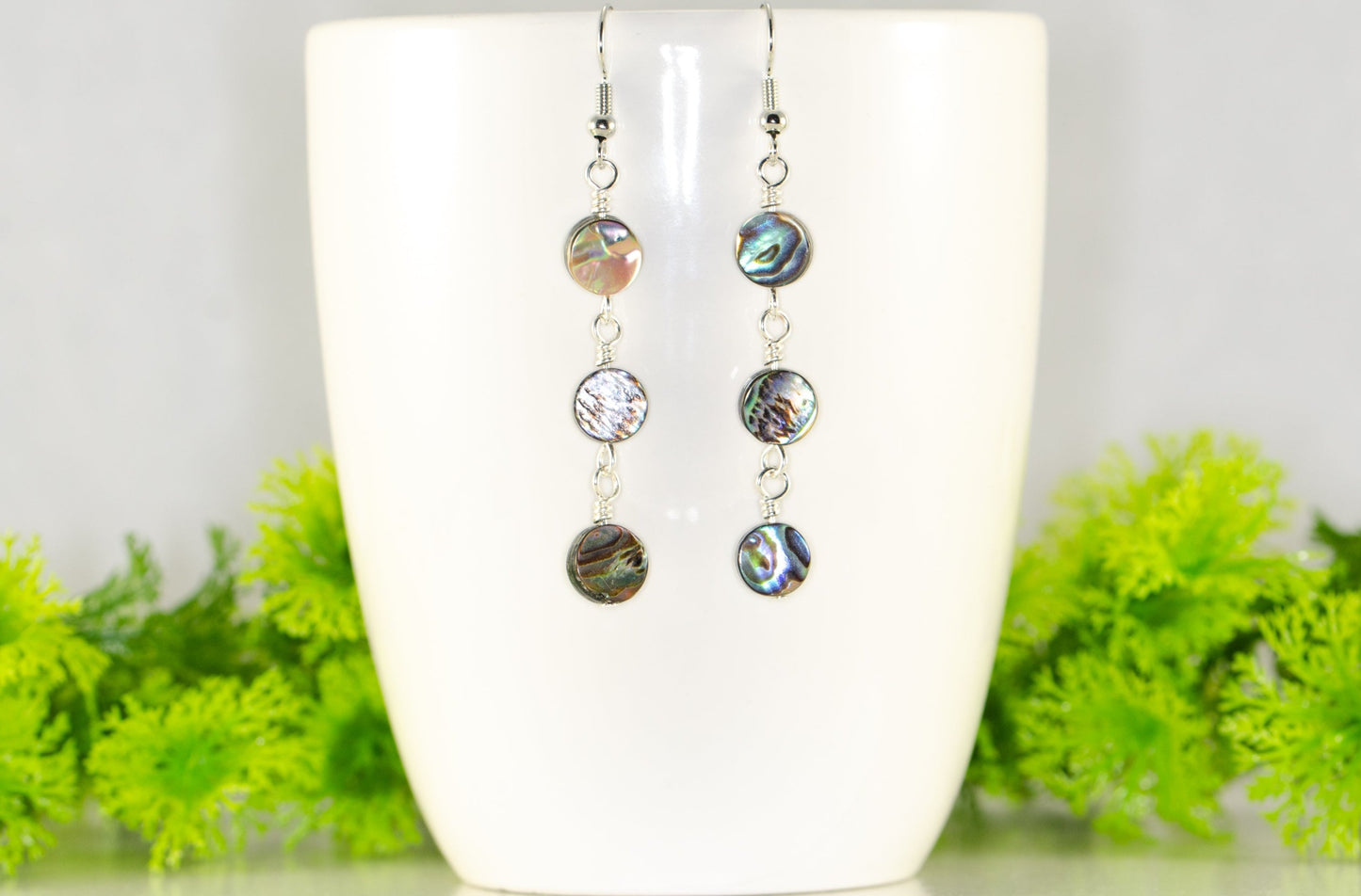Elegant Long Natural Abalone Shell Earrings displayed on a coffee mug.